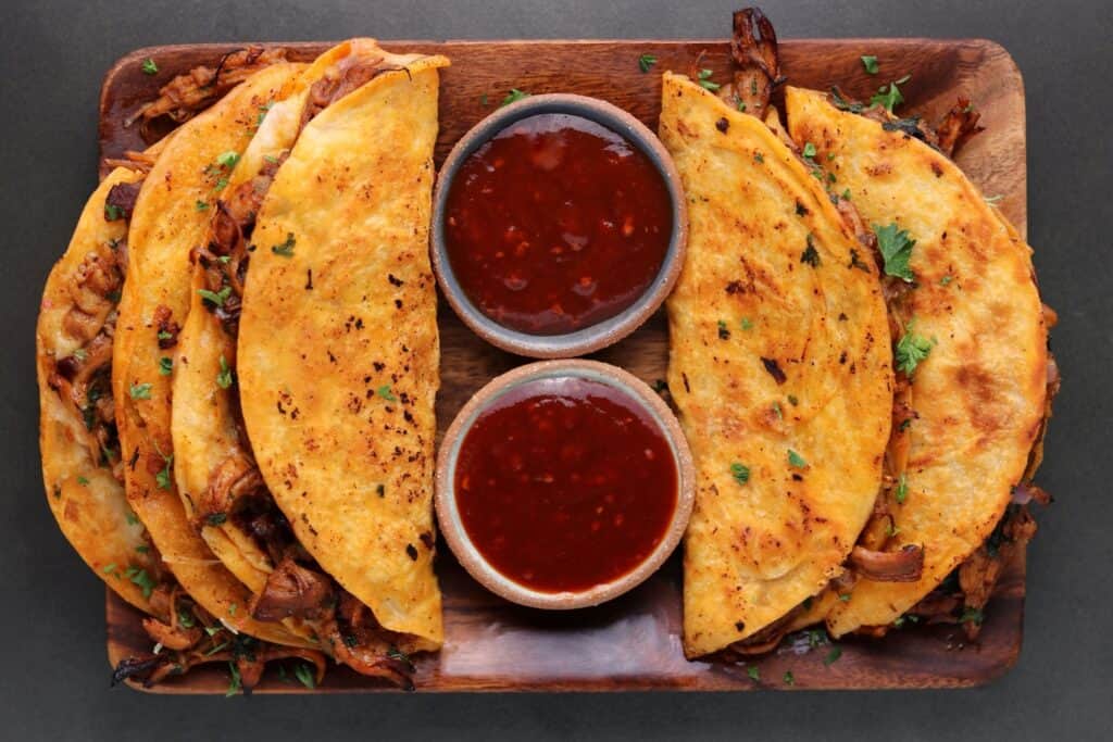 four bbq chicken quesadillas on a wooden tray with two bowls of bbq sauce