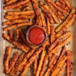 roasted carrot sticks on a parchment lined sheet pan with ketchup