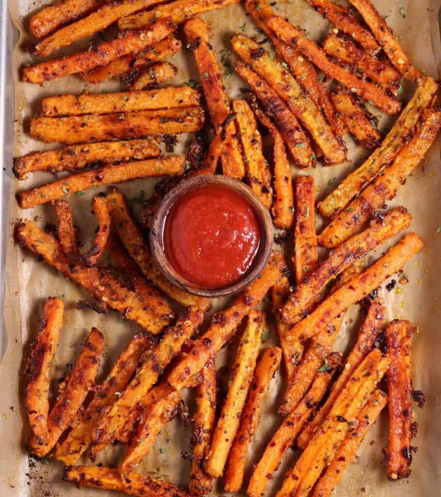 roasted carrot sticks on a parchment lined sheet pan with ketchup