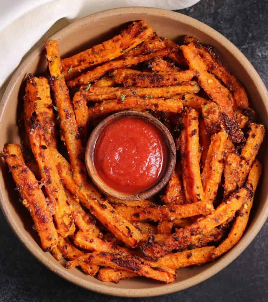 carrot sticks in a brown bowl with a small bowl of ketchup in the center
