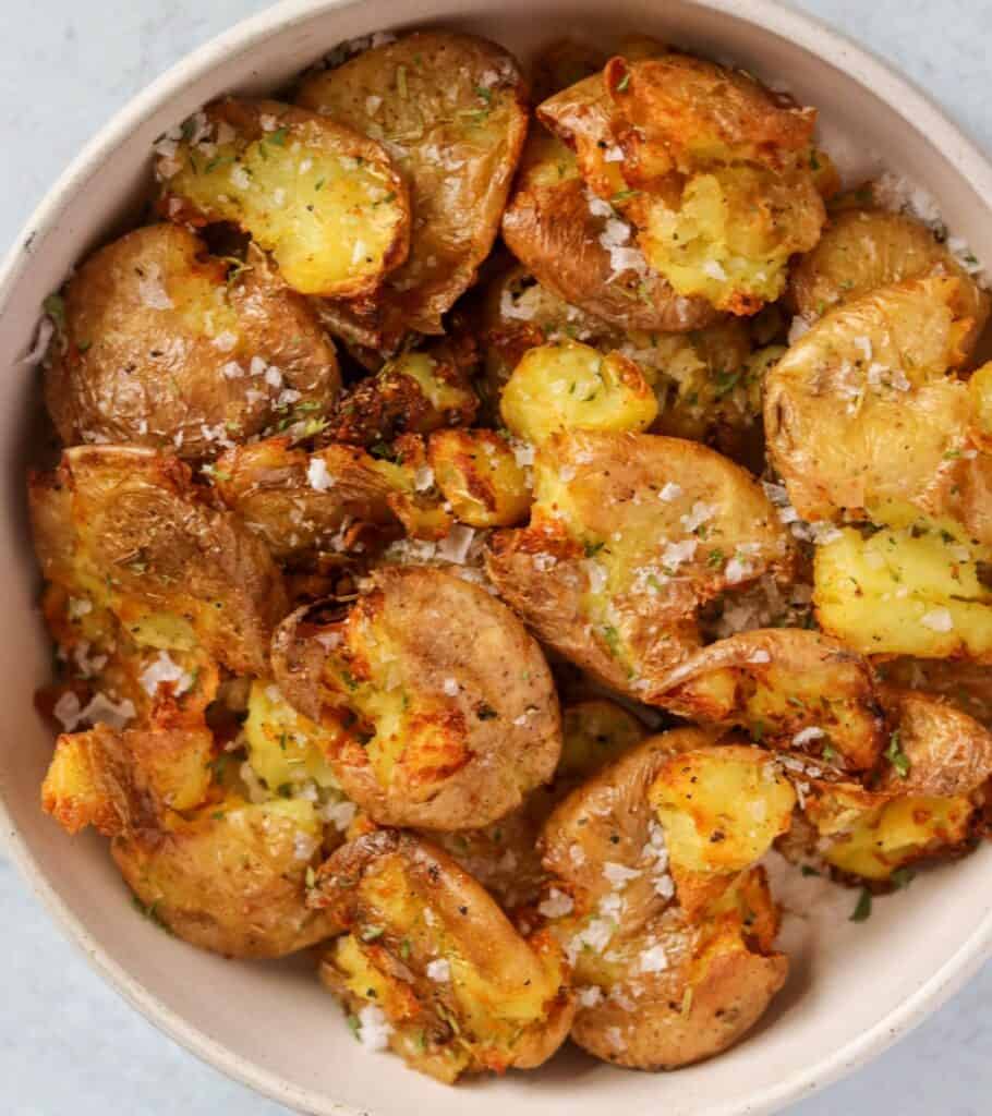golden brown smashed potatoes in a bowl topped with flaky salt 