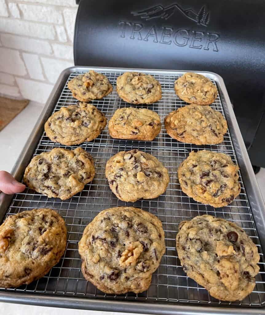 holding a sheet pan with smoked chocolate chip cookies in front of a Traeger grill