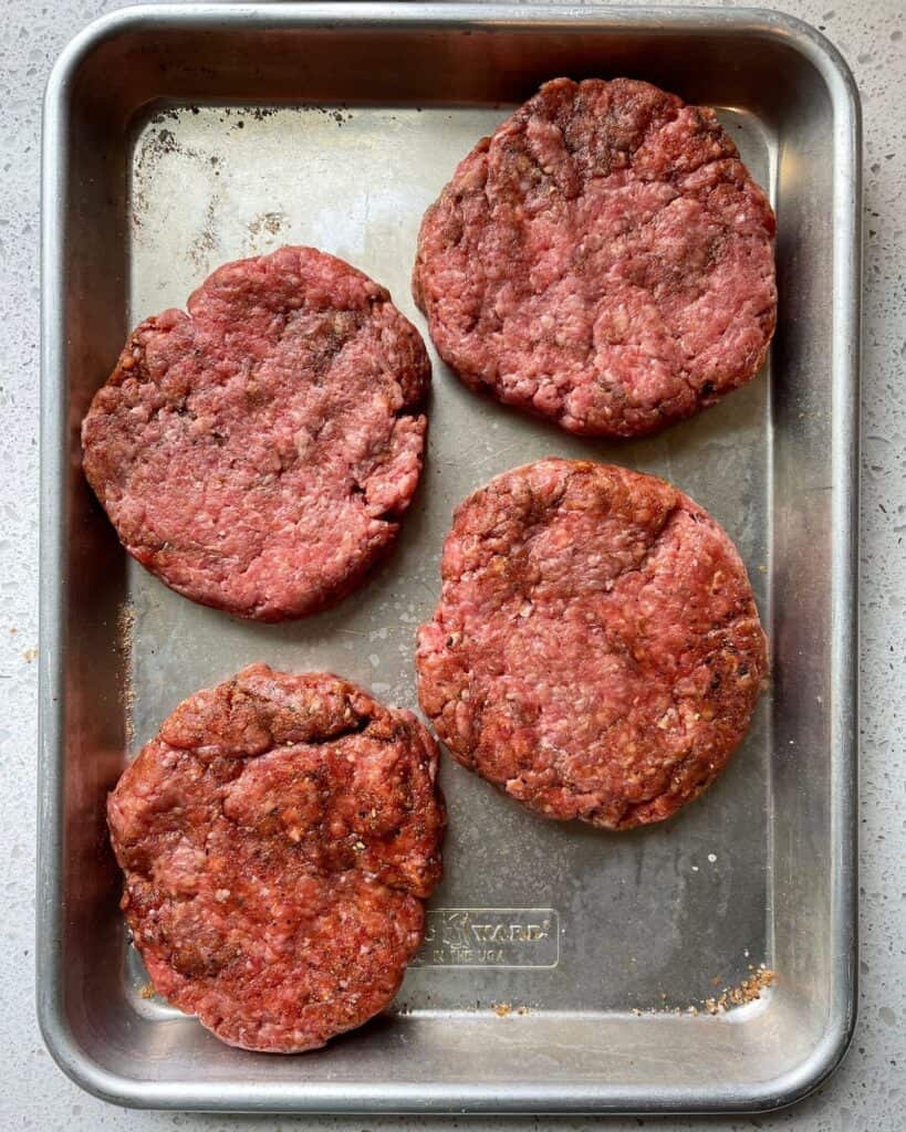 four burger patties formed on a quarter sheet pan before going in the smoker