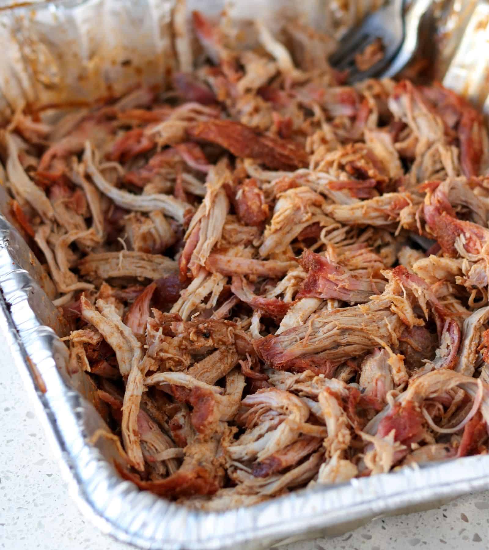 pulled pork loin in an aluminum tray with forks