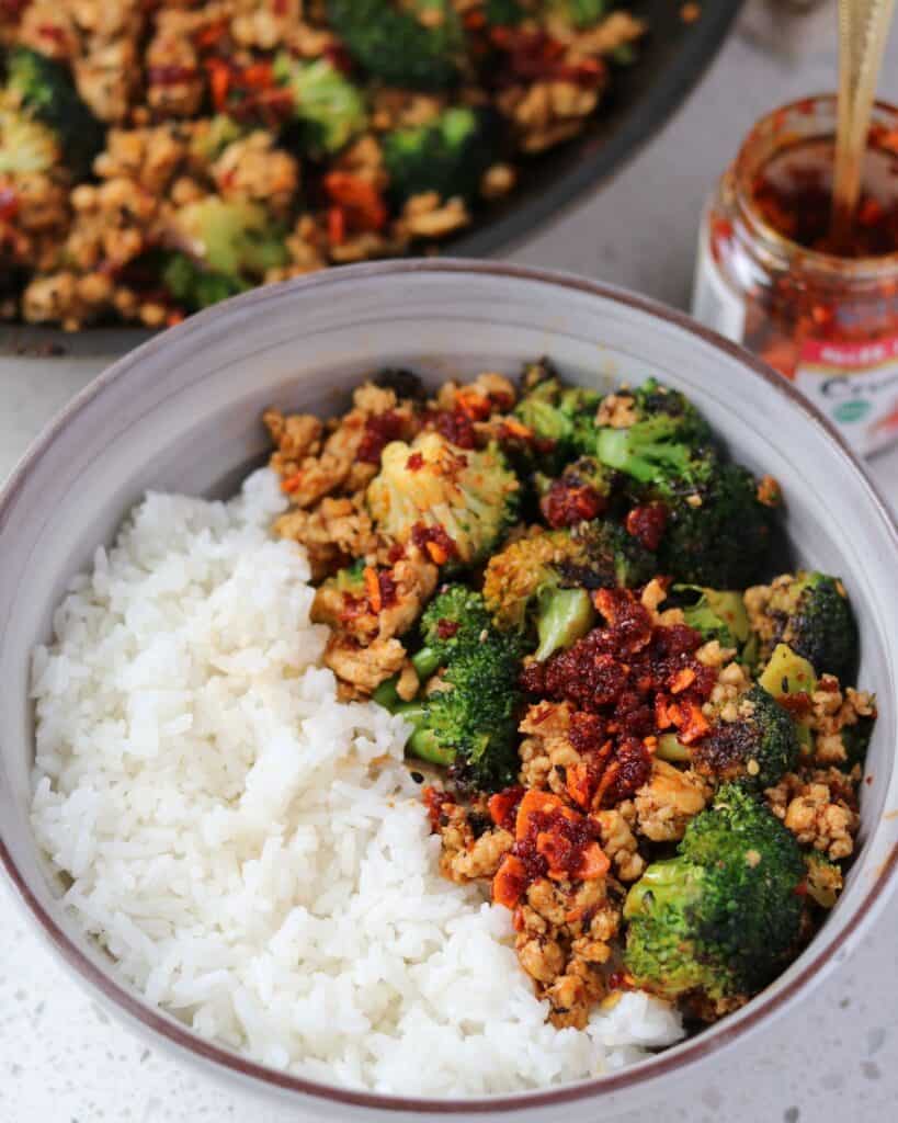 ground chicken and broccoli topped with chili crisp in a bowl with rice 