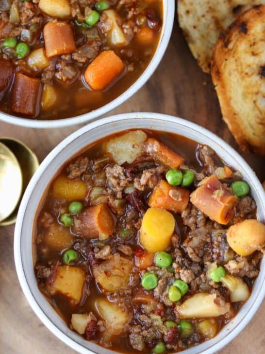 two bowls of vegetable beef soup with grilled bread on the side