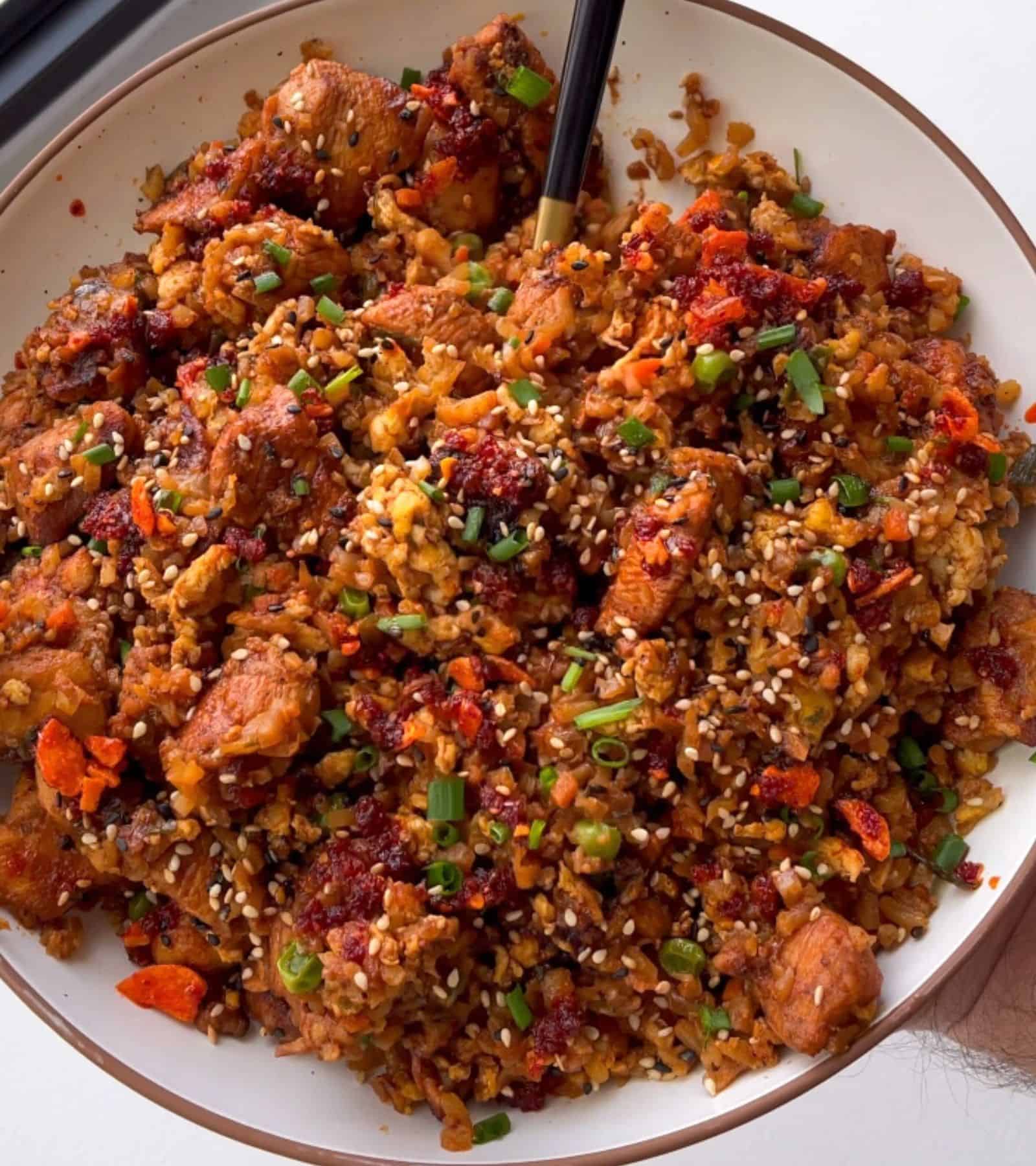 bbq chicken fried cauliflower rice garnished with chives, sesame seeds, and chili crisp