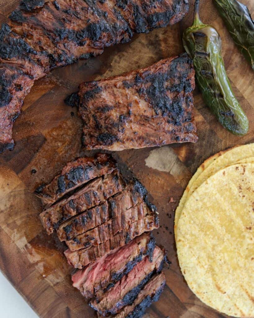 sliced beef fajitas on a cutting board with tortillas and grilled jalapeño peppers