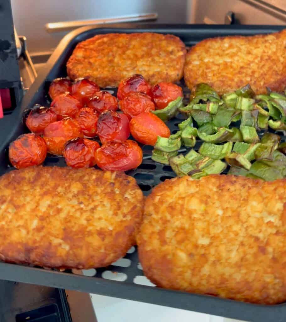 four hash brown patties on an air fryer basket with tomatoes and jalapeño pepper