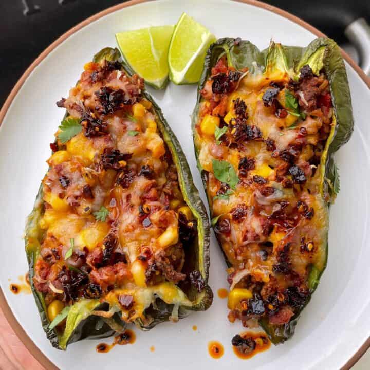 two Mexican stuffed poblano peppers on a plate in front of a Traeger grill