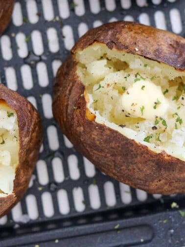 baked potatoes on an air fryer basket with butter and seasonings