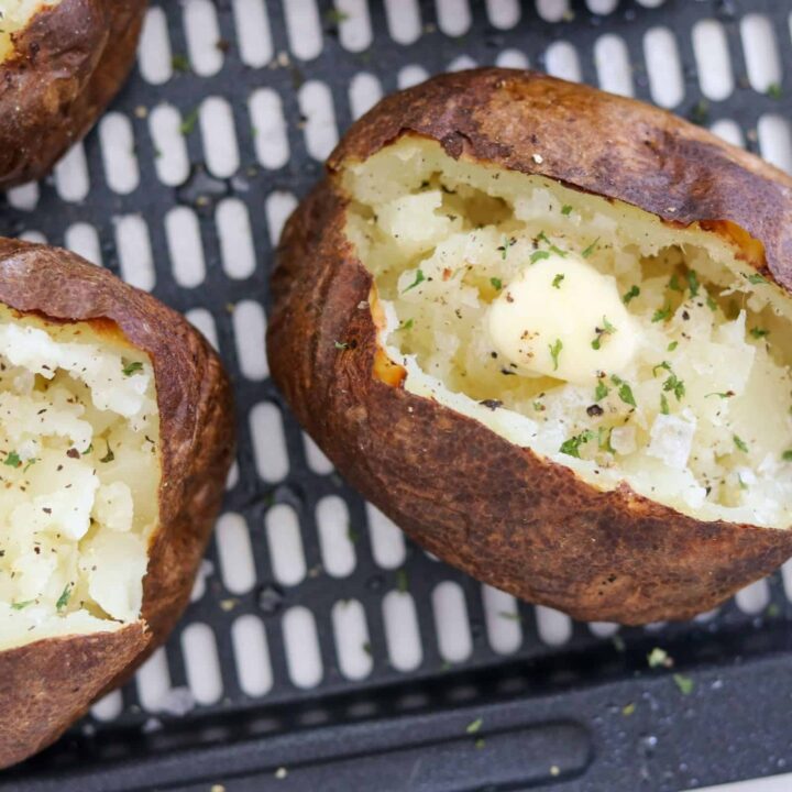baked potatoes on an air fryer basket with butter and seasonings