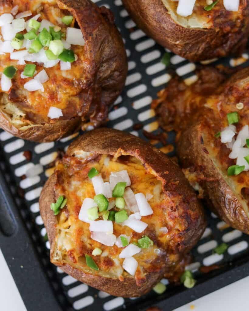 air fryer baked potatoes topped with chili, cheese, diced onion, and jalapeño