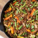 firecracker ground beef, green beans, bell pepper, and onion in a skillet with a scallion and sesame seed garnish
