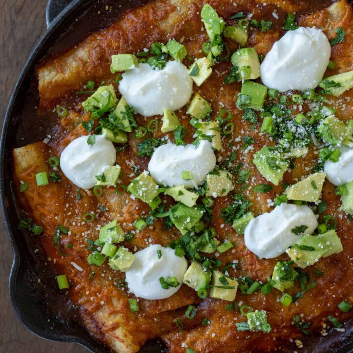 smoked enchiladas in a cast iron skillet garnished with diced avocado, cilantro and scallions, and sour cream
