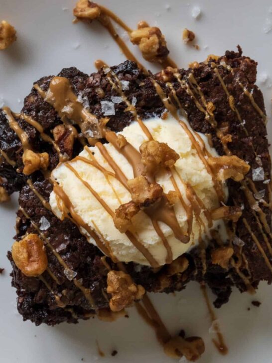 smoked brownie on a plate topped with vanilla ice cream, smoked walnuts, and a cookie butter drizzle