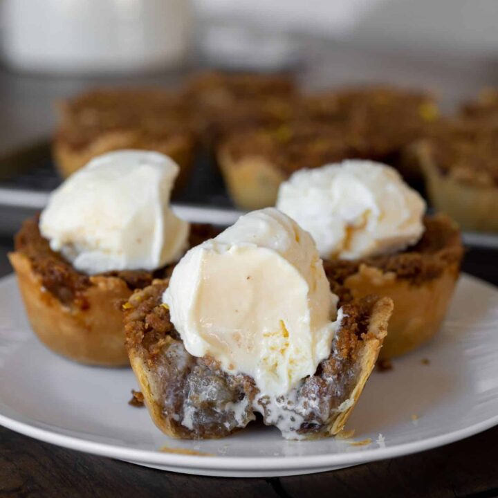 three mini apple pies with ice cream on top. front pie has a bite taken out of it.