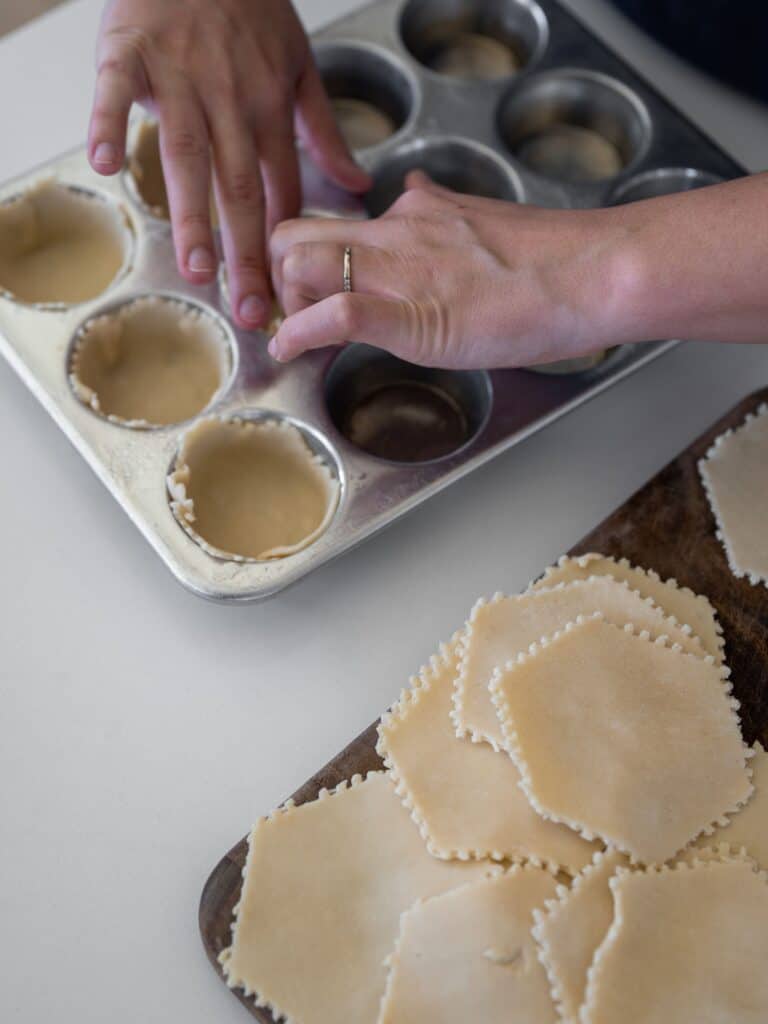 Mini pie crusts being added to the muffin tin.