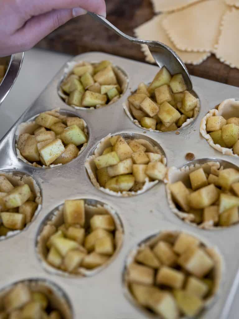 Apple pie filling being added to the pie crusts in the muffin tin.
