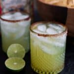 two sparkling margaritas in glasses with salted rims beside of a bowl of tortilla chips and a bottle of tequila