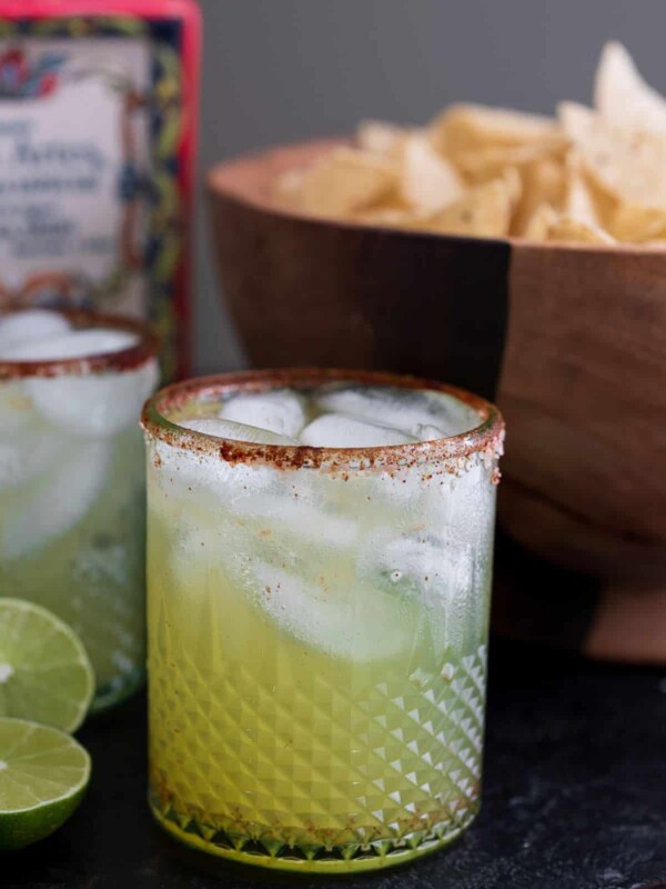 two sparkling margaritas on a table with tortilla chips and a bottle of tequila