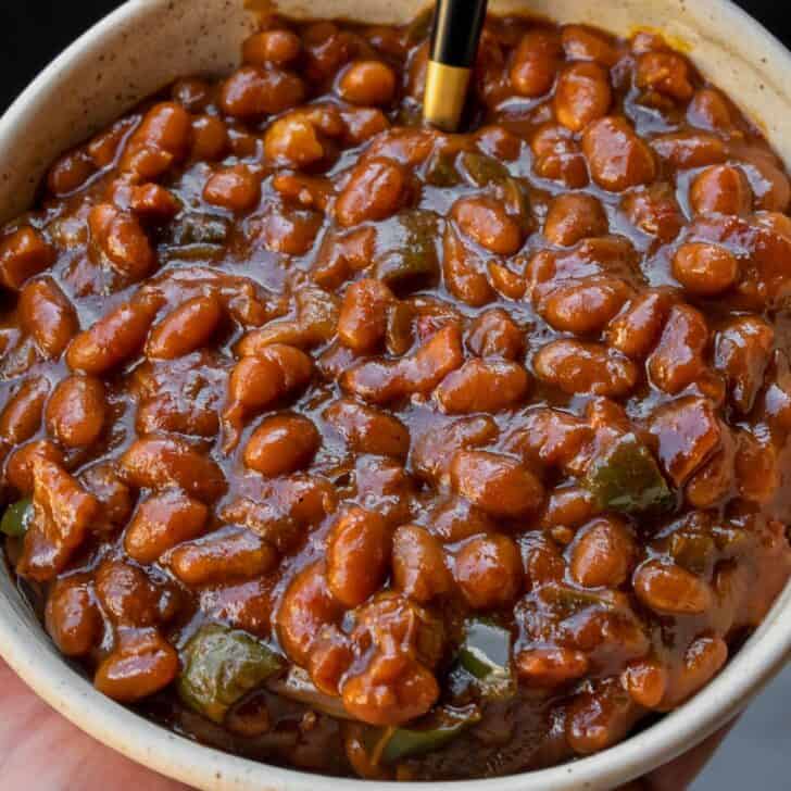 holding a bowl of smoked baked beans in front of a Traeger grill
