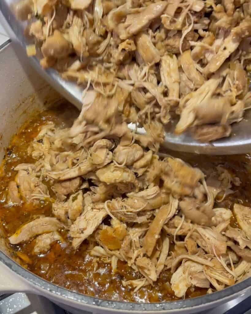 adding pulled chicken to the sauce in the Dutch oven