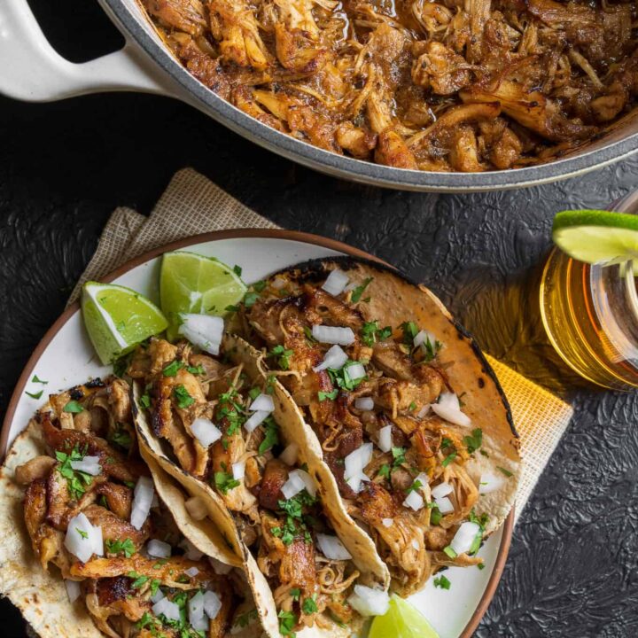 three chicken tacos beside a Dutch oven with pulled Mexican chicken