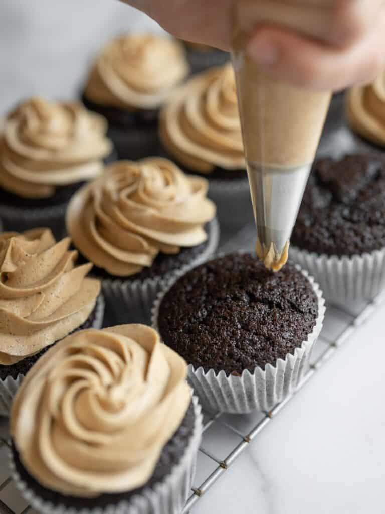 Espresso cupcakes with espresso buttercream being piped on top.