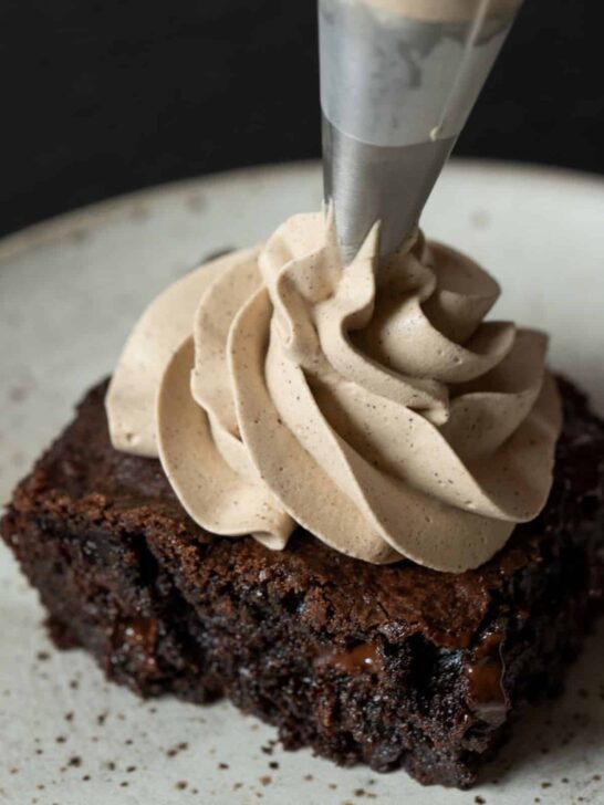A brownie slice with espresso whipped cream being piped on top.