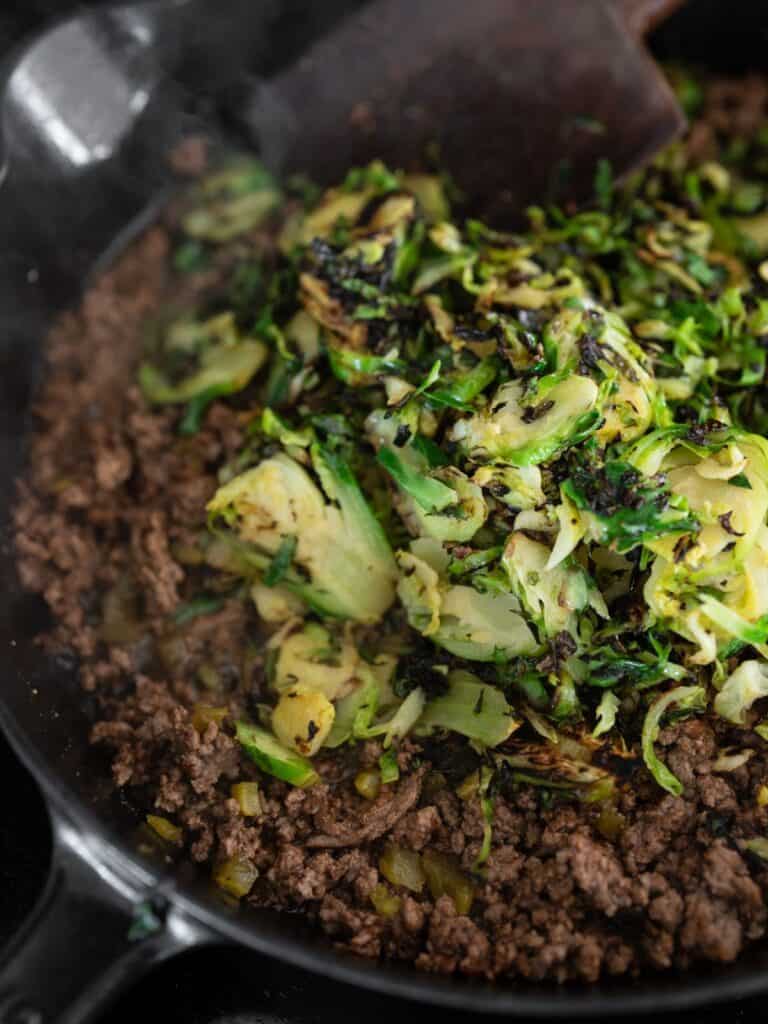 cooked shaved brussels sprouts in the skillet with the cooked ground beef and lime vinaigrette