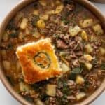 ground beef and potato soup in a brown bowl with cornbread