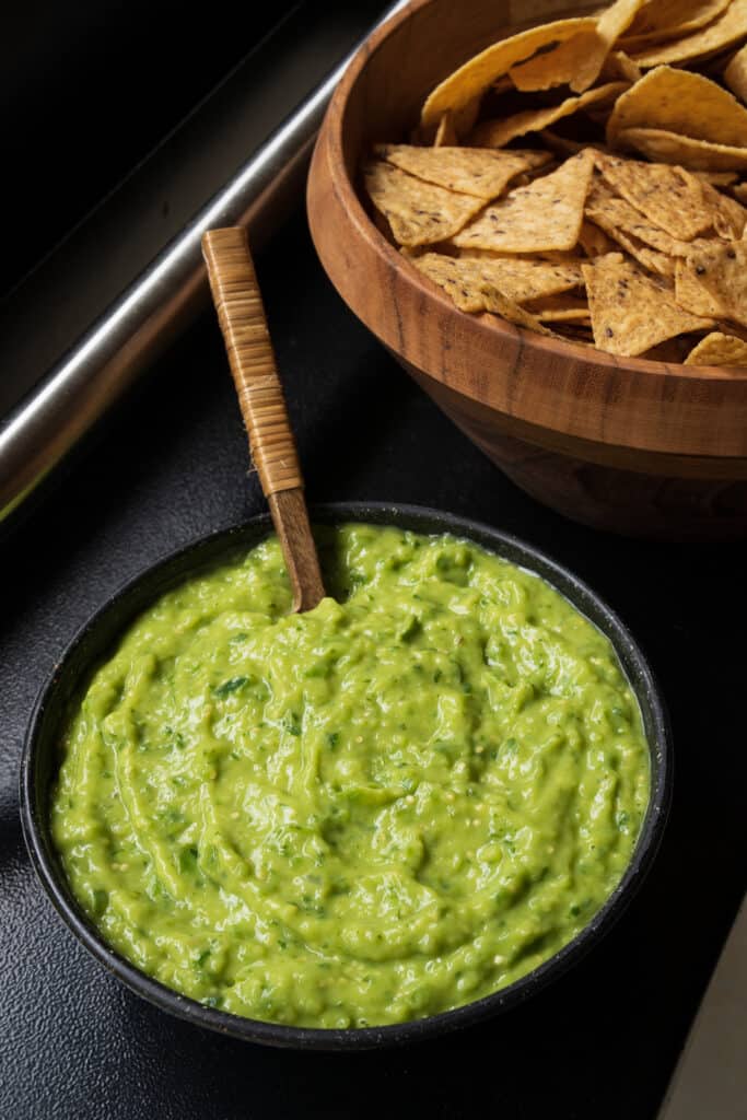 smoked guacamole salsa in a bowl on a Traeger grill beside a bowl of tortilla chips