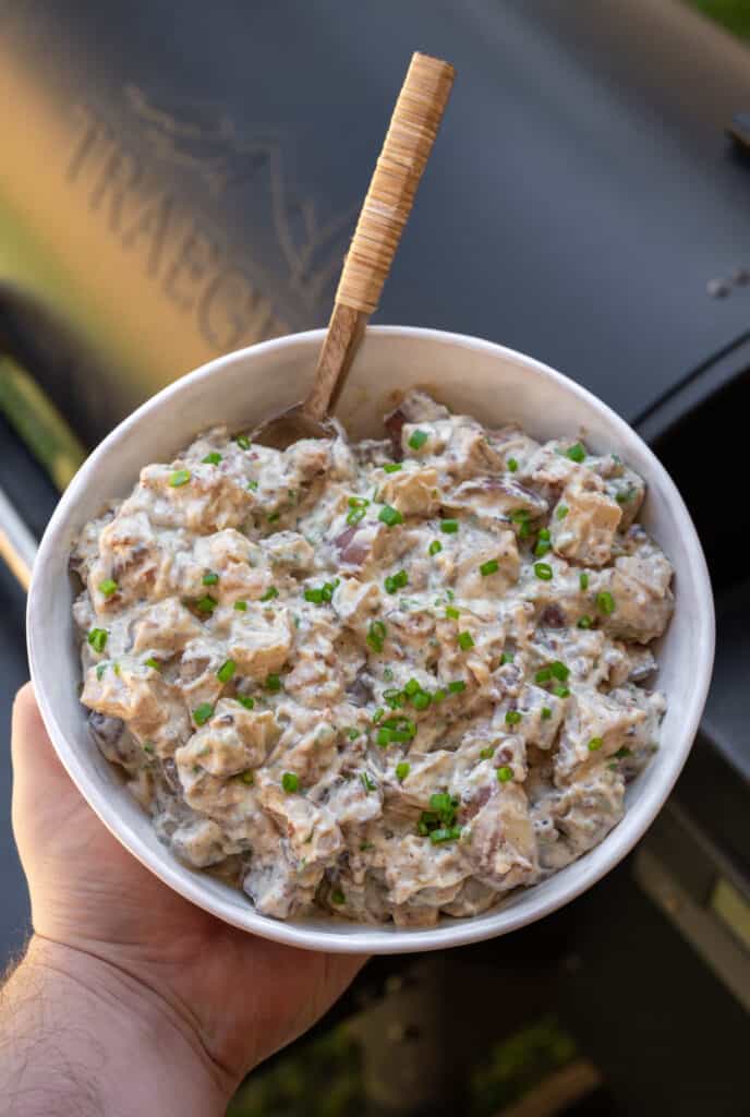 holding a bowl of smoked potato salad next to a Traeger grill