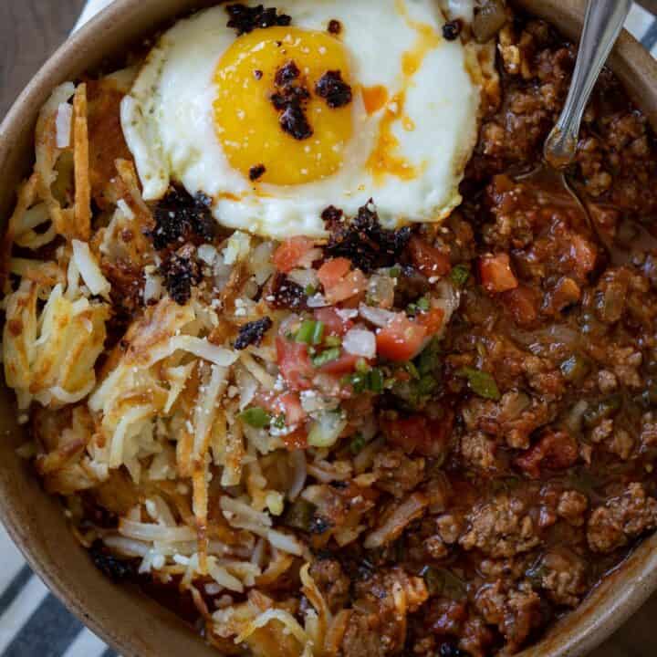 breakfast chili in a bowl with a fried egg, hash browns, and pico de gallo