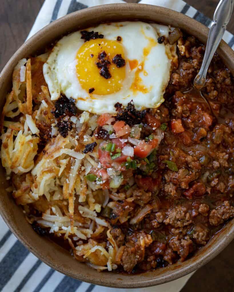 breakfast chili in a bowl with a fried egg, hash browns, and pico de gallo