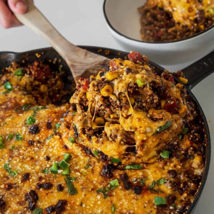 wooden serving spoon in a cast iron skillet filled with cheesy Tex Mex quinoa and ground beef