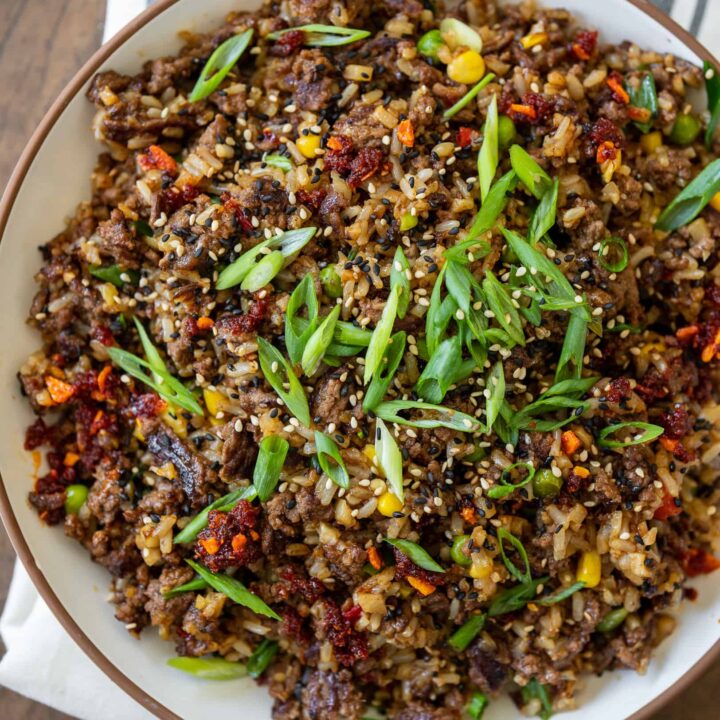 large serving bowl filled with ground beef fried rice garnished with chili crisp, sesame seeds, and scallions