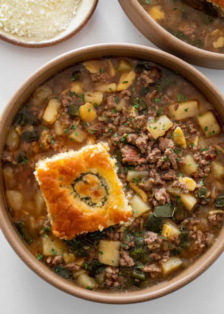 ground beef and potato soup in a brown bowl with cornbread