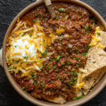 ground bison chili in a bowl with sour cream, cheddar cheese, and tortilla chips