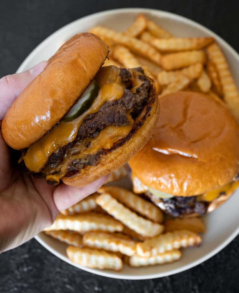 holding a ground bison burger above a plate of crinkle cut fries