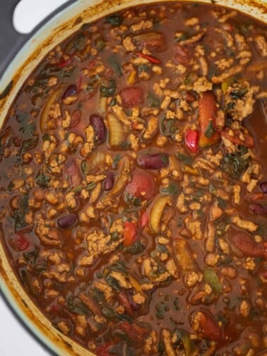 ground pork chili in a Dutch oven with a wooden spoon in it