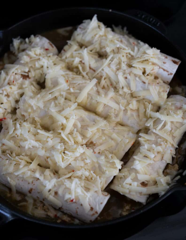ground turkey enchiladas topped with shredded cheese before baking in a skillet