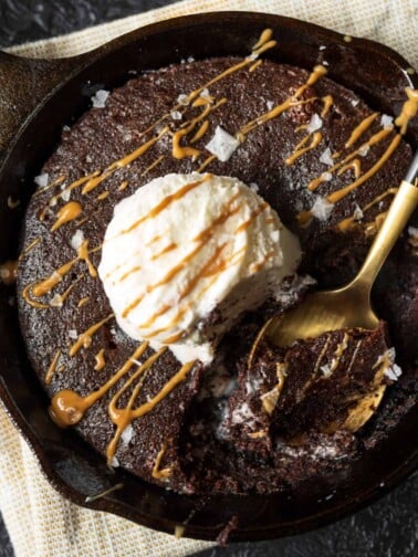 golden spoon in a cast iron skillet brownie with ice cream and a cookie butter drizzle