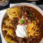 Traeger smoked chili in a bowl with sour cream, cheese, pico, salsa macha, and tortilla chips