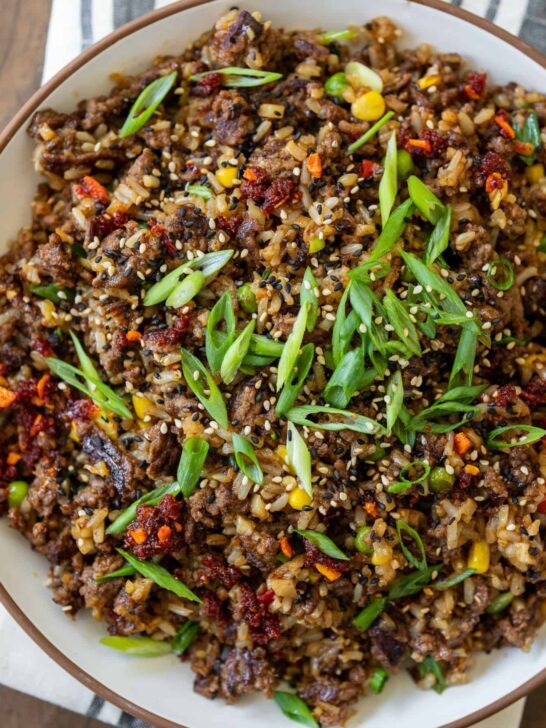 large serving bowl filled with ground beef fried rice garnished with chili crisp, sesame seeds, and scallions