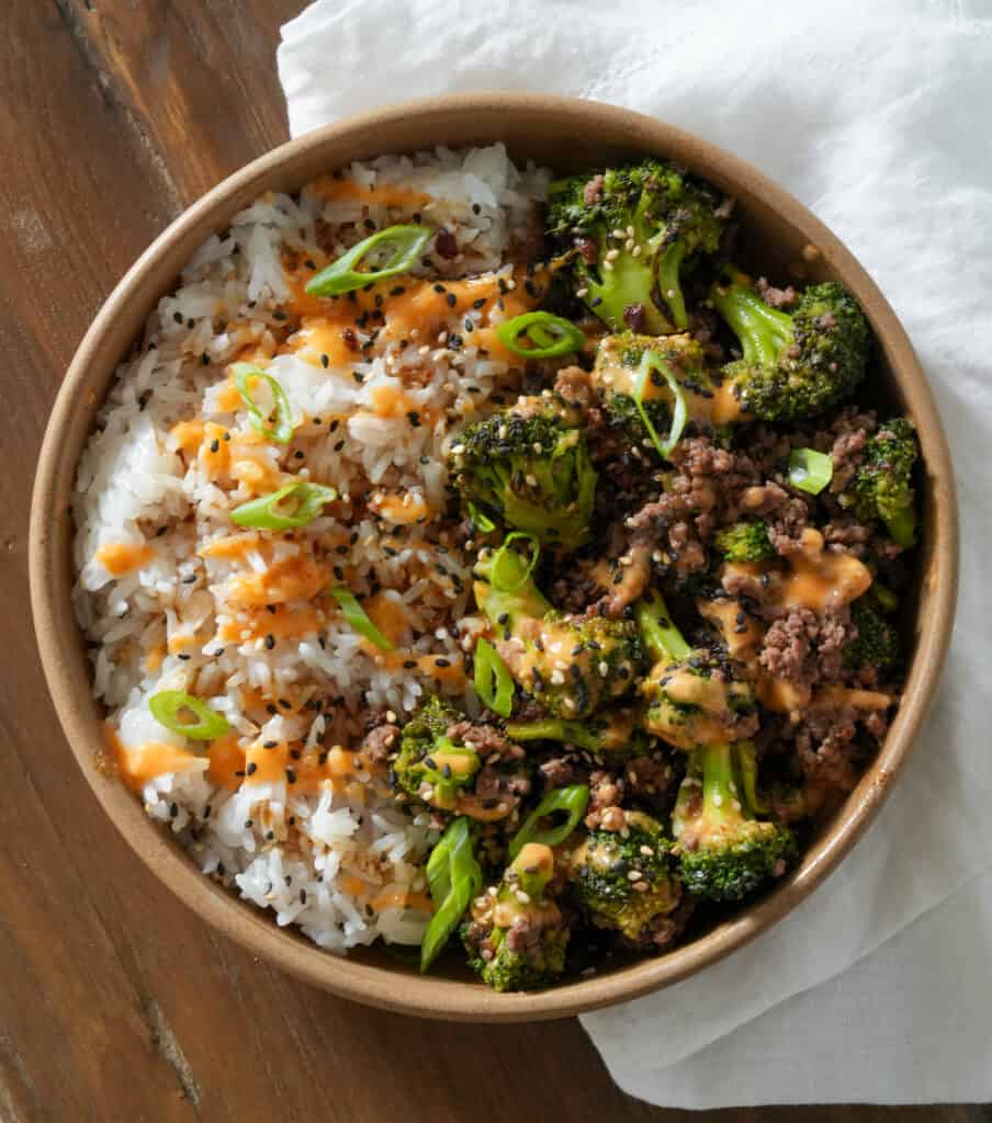 teriyaki ground beef and broccoli in a bowl with rice, sauce, and sesame seeds