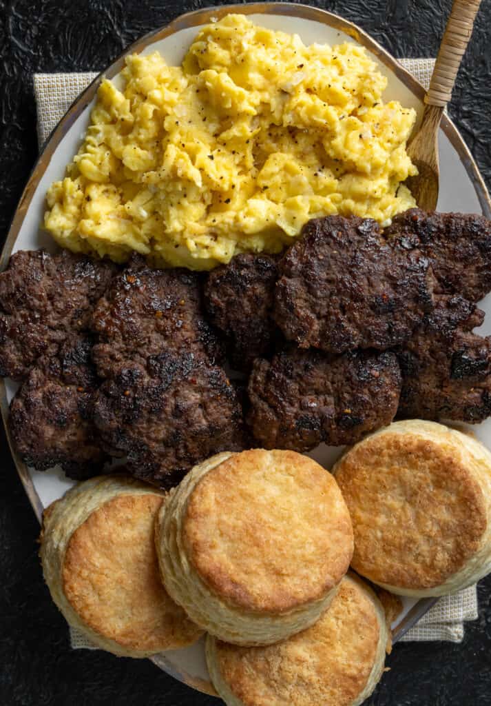 ground bison breakfast sausage patties on a plate with buttermilk biscuits and scrambled eggs