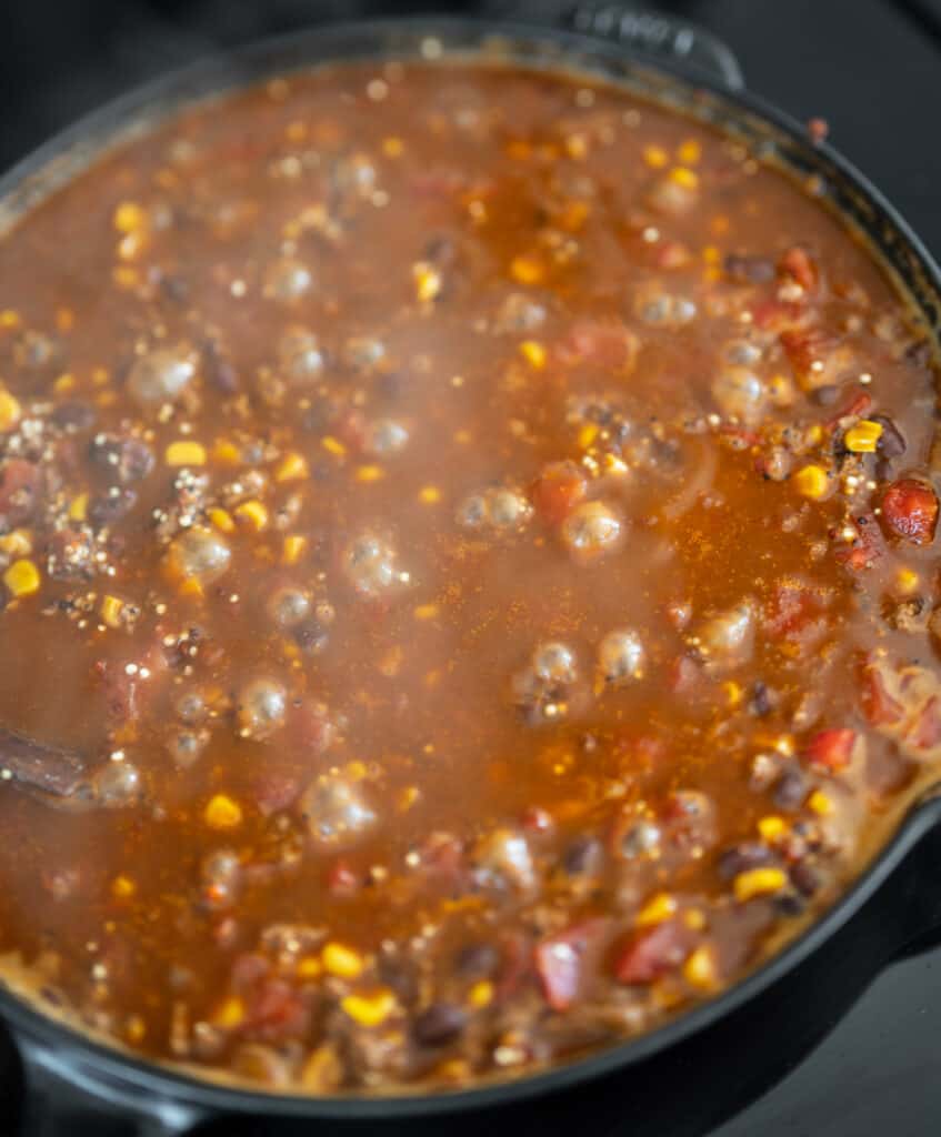 quinoa and ground beef with beef broth simmering in a cast iron skillet