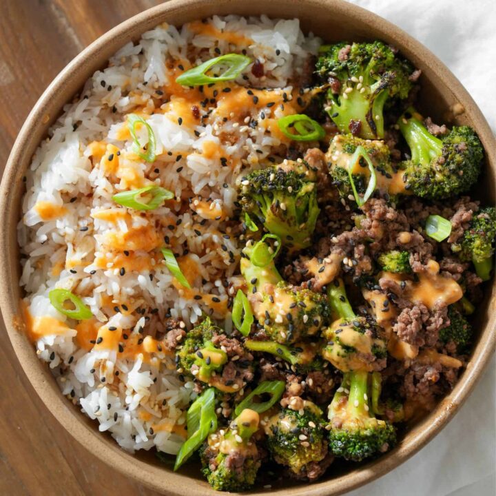 teriyaki ground beef and broccoli in a bowl with rice, sauce, and sesame seeds